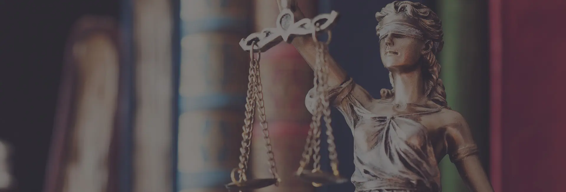 Estátua da Justiça com balança diante de estante de livros jurídicos